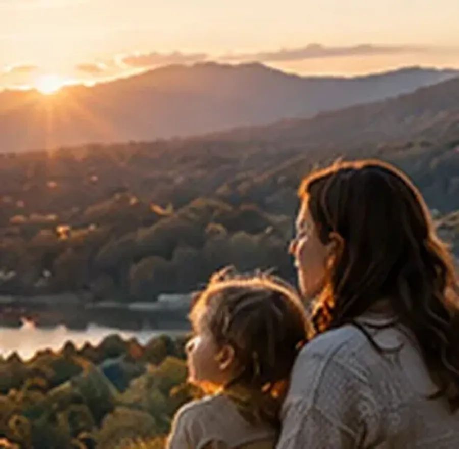 A parent and child looking out over a valley at sunset